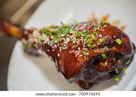 Sweet and sour turkey drumstick seasoned with roasted sesame seed and green onions, could also pass as chicken or other bird. Served on a simple white plate. Close focus and closeup picture.