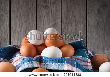 Fresh chicken brown and white eggs on plaid linen napkin with hay at rustic wood table. Rural still life, natural healthy food and organic farming concept.