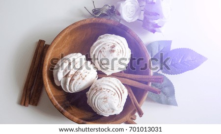 Marshmallows in a wooden plate surrounded by red berries on a light background