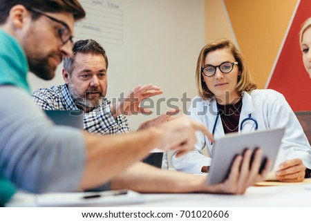 Group of healthcare workers with digital tablet meeting in hospital boardroom. Medical staff during morning briefing. Royalty-Free Stock Photo #701020606