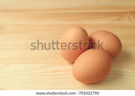 Three fresh uncooked hen eggs isolated on the wooden table, with free space for text and design 