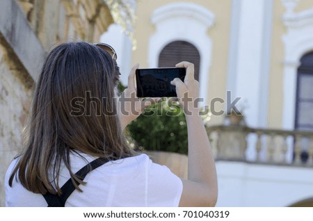 A rear view of a young woman with sunglasses photographing an ancient building in nature with a blurred background