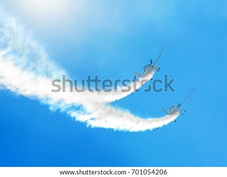 Two white turboprop airplane with a trace of white smoke against a blue sky