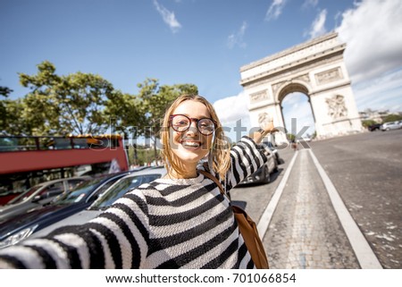 Young woman tourist making selfie portrait with famous Triumphal Arch on the background in Paris