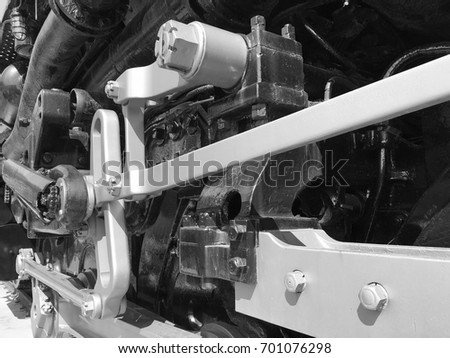 Close up angled photo of lower part of antique train engine in black and white showing mechanical parts