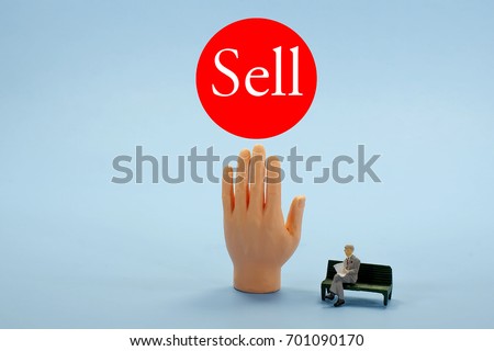 This photo is a financial concept of selling stocks, oil, gold, real estate or other commodities, in a bear market.  Hand reaching for sell button on blue background with man reading a newspaper.