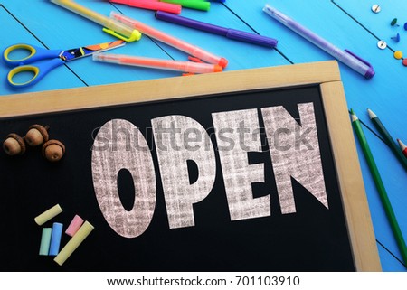 The text Open on a black chalkboard on the table with school accessories (pens, pencils, brushes)
