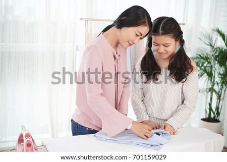 Mother teaching her daughter how to fold shirts after ironing