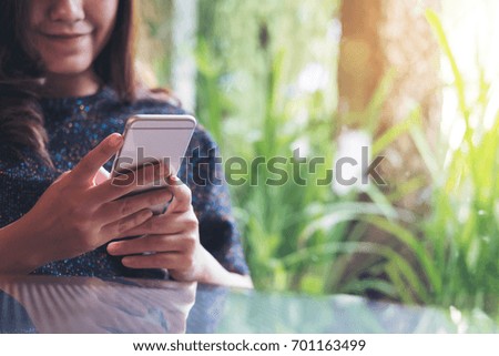 A beautiful Asian woman using and looking at smart phone in modern cafe with green nature background