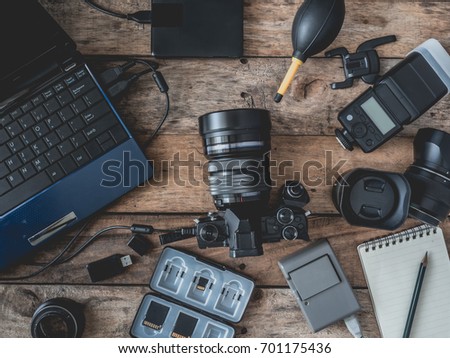 top view of work space photographer and travel concept with digital camera, battery charger camera, memory card storage box, external harddisk, flash, computer laptop on wooden background