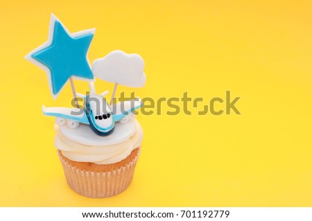 Cupcake for boy with whipped cream, decorated plane, toppers star and cloud on yellow background. Picture for a menu or a confectionery catalog.