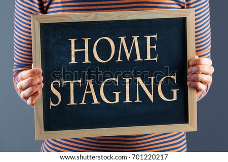 Female hands holding small black chalkboard in front of the body closeup with words Home Staging. On gray background with copy space Royalty-Free Stock Photo #701220217