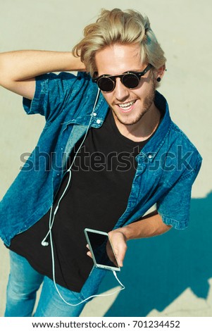 Vacation, relaxation, passion concept. Young fashionable blonde in sunglasses man relaxing, listening to music and enjoying beautiful, sunny weather. Outdoor shot