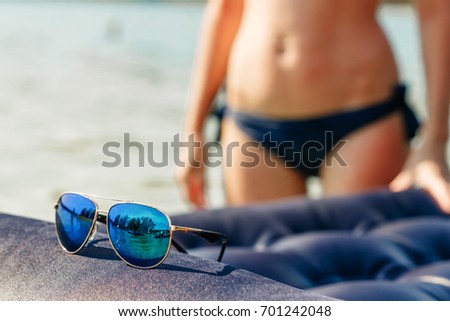 Beautiful sunglasses in gold rim against the background of a blurred girl in a bikini. The concept of vacation, vacation, summer, vacation, travel. Copy space.