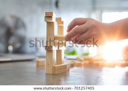Hand of kid playing a blocks wood tower game of architectural project with sun flare and blur background .Selected focusing . Royalty-Free Stock Photo #701257405