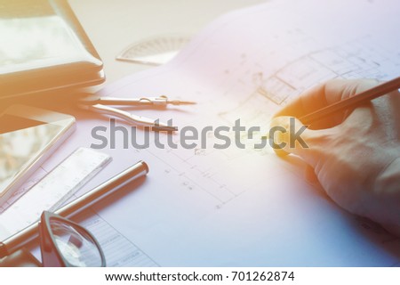 Man hand editing blueprint with Divider, pencil, pen, ruler, glasses and smartphone and blueprint on table top.Table top view of Engineers table at office workplace.selective focus.
