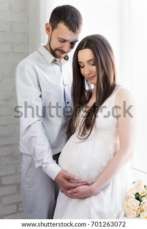family and parenthood concept - happy pregnant couple in front of the window