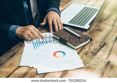 businessmen using laptop analyzing marketing strategy with statistic graph and notebook on wooden desk.