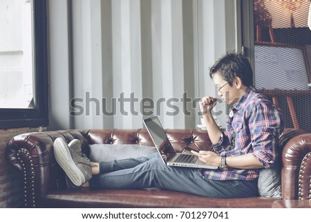 Young Asian businessman using tablet computer in classy coffee shop.Interior of coffee shop with customer using digital devices on free wifi internet service.