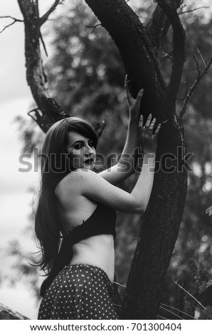 a young girl in a red wig is on crooked tree . the contrast of youth and age. black white photo