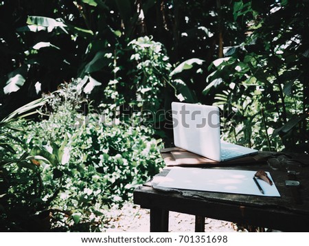 Businesses happen everywhere, just have inspiration. The picture of white laptop, paper, pencil, watch and glasses on green forest background in the afternoon.  selective focus