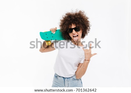 Young crazy woman showing rock gesture while standing and holding skateboard isolated over white background