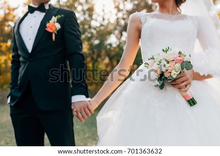 Wedding bouquet. Blurred bride with in a white dress and groom in tuxedo are holding hands. Soft focus on flowers. Outdoors ceremony