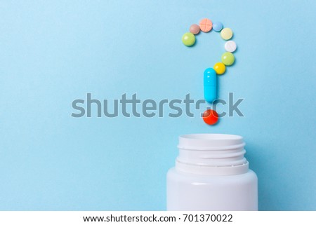 Assorted pharmaceutical medicine pills, tablets and capsules symbol question mark on a blue background. Copy space for text