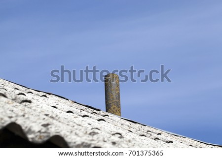 old chimney installed on the roof of a building covered with slate. Photo close-up on a background of blue sky. On the pipe grows lichen yellow