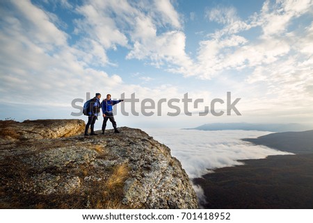 Two climbers standing on top of summit above clouds in the mountains. Hiker man pointing with his hand discussing route. Plan, vision and mission concept. Royalty-Free Stock Photo #701418952