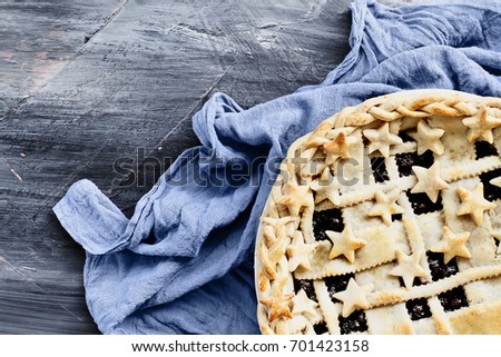 Top view of a blueberry pie with lattice and stars crust with grey napkin over an industrial artistic wooden background.