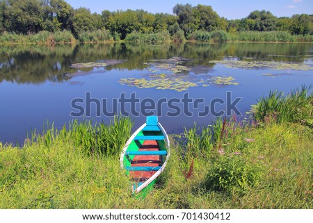 The picture was taken in Ukraine, on the South Bug river. In the picture a fishing boat moored to the river bank. In the background, another bank of the river is visible. 