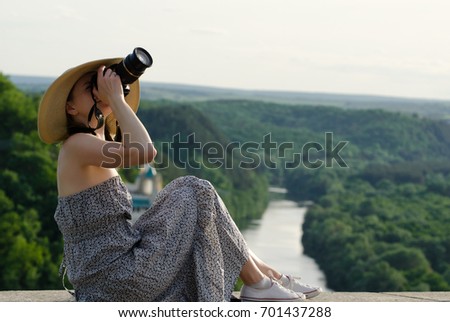 Girl sits and takes pictures against the background of forest and meandering river