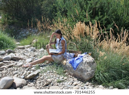 A beautiful young woman is having a picnic near the river