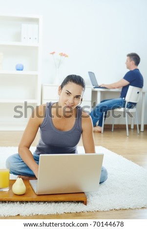Young woman sitting on floor at home using laptop computer, smiling.?
