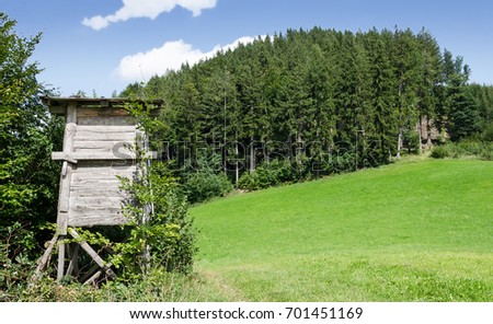 Wooden deer stand along the edge of a meadow, horizontal view. Tree or box stand. Enclosed platform. Elevates the hunter for better vantage point, keeps him hidden. Heuberg, Salzburg, Austria. Photo.