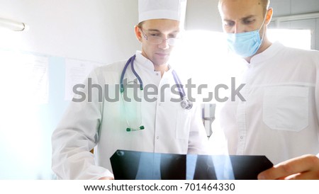 Medical workers in hospital office examine x-ray prints. Male medics consult with each other while looking at x ray image. Two caucasian doctors view mri picture and discussing about it. Close up.