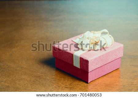 Red gift box decorated with golden ribbon on wooden background for giving in holidays,image with color filter