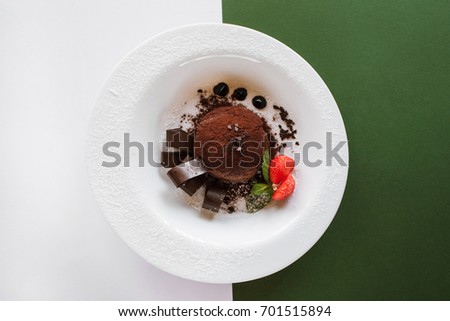 Chocolate fondant on contrast colorful background of white and green. Delicious dessert with decoration from strawberry and mint serving in restaurant, top view with free space