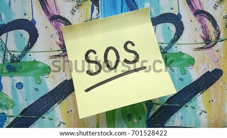 Underlined "SOS" word written on a yellow sticky note on colorful background
