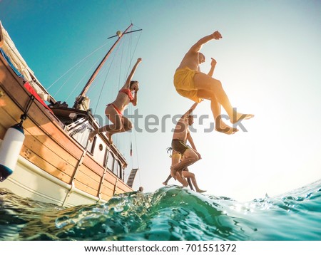 Happy friends diving from sailing boat into the sea - Young people jumping inside ocean in summer excursion day - Vacation, youth and fun concept - Soft focus on left man - Fisheye lens distortion Royalty-Free Stock Photo #701551372