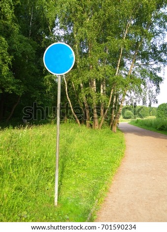 Road sign permissive, warning, blue in a white circle stands in the countryside near the path, road, in the forest.