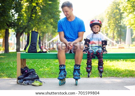 Portrait of cute baby boy with inline skating instructor in the park.