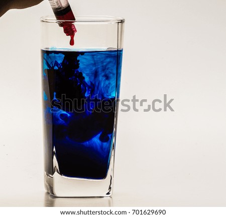 Blue food coloring diffuse in water inside glass with empty copyspace area for slogan or advertising text message, over isolated grey background. 