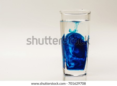 Blue food coloring diffuse in water inside glass with empty copyspace area for slogan or advertising text message, over isolated grey background. 