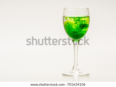 Green food coloring diffuse in water inside wine glass with empty copyspace area for slogan or advertising text message, over isolated grey background. 