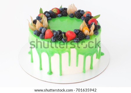 Birthday cake in green glaze, decorated with strawberries, blueberries and blackberry on white background. Picture for a menu or a confectionery catalog. 