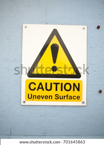 a close up caution uneven surface sign on blue wall seafront; England; UK
