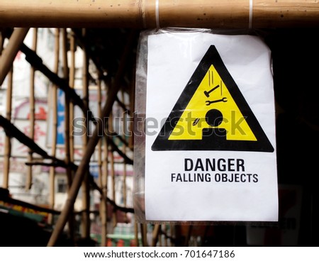 A warning sign hanging on a pole at a construction site. The words "Danger Falling Objects" are written on it.