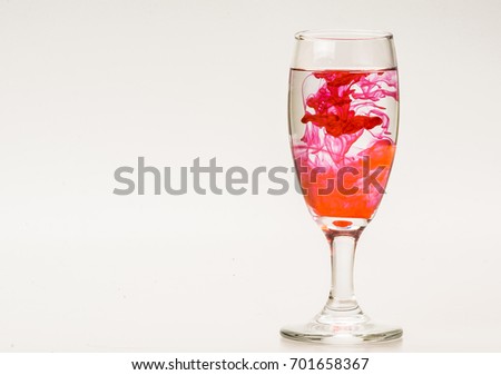 mixture of food coloring diffuse in water inside wine glass with empty copyspace area for slogan or advertising text message, over isolated grey background. 